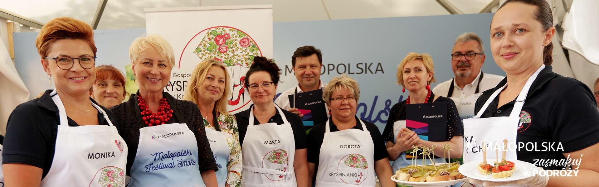 Grupa kobiet i mężczyzn w fartuchach na stoisku na Małopolskim Festiwalu Smaku, wśród nich Iwona Gibas