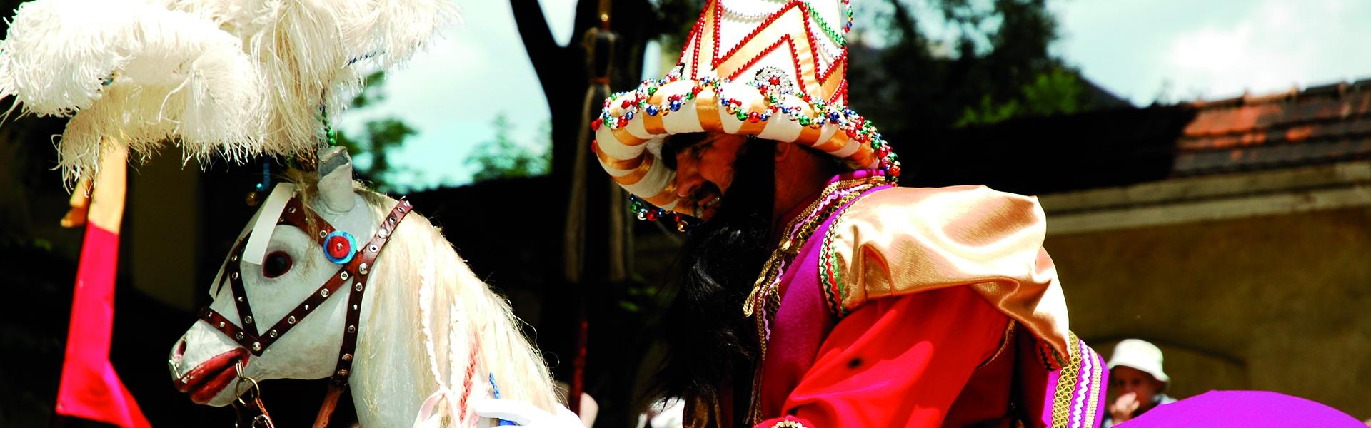 Lajkonik with raised mace in colourful Asian costume in Kraków’s Main Market Square, with people and the towers of the Gothic Church of St Mary in the background.